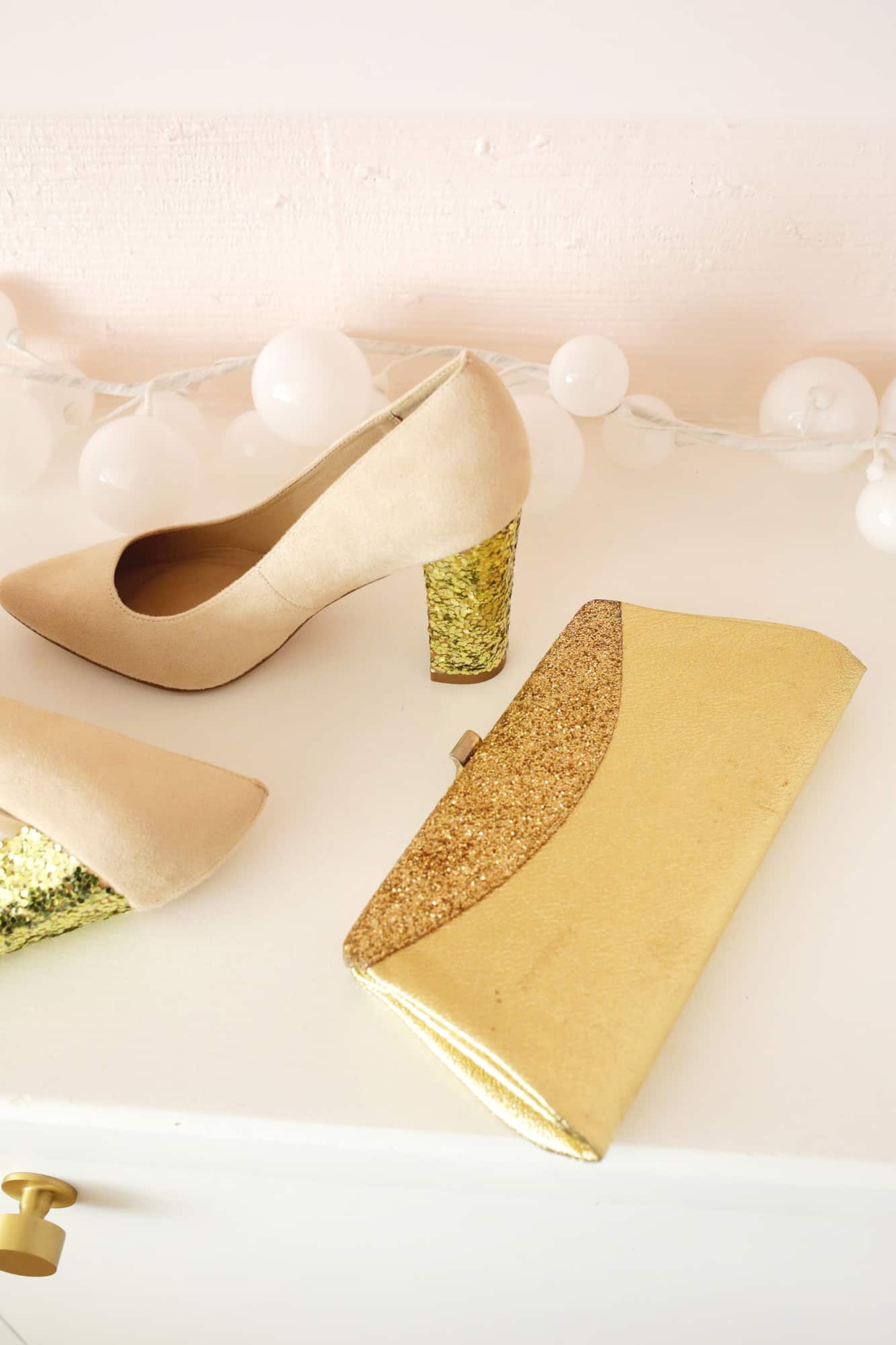Shoes with gold glittered heels next to gold bag with glitter
