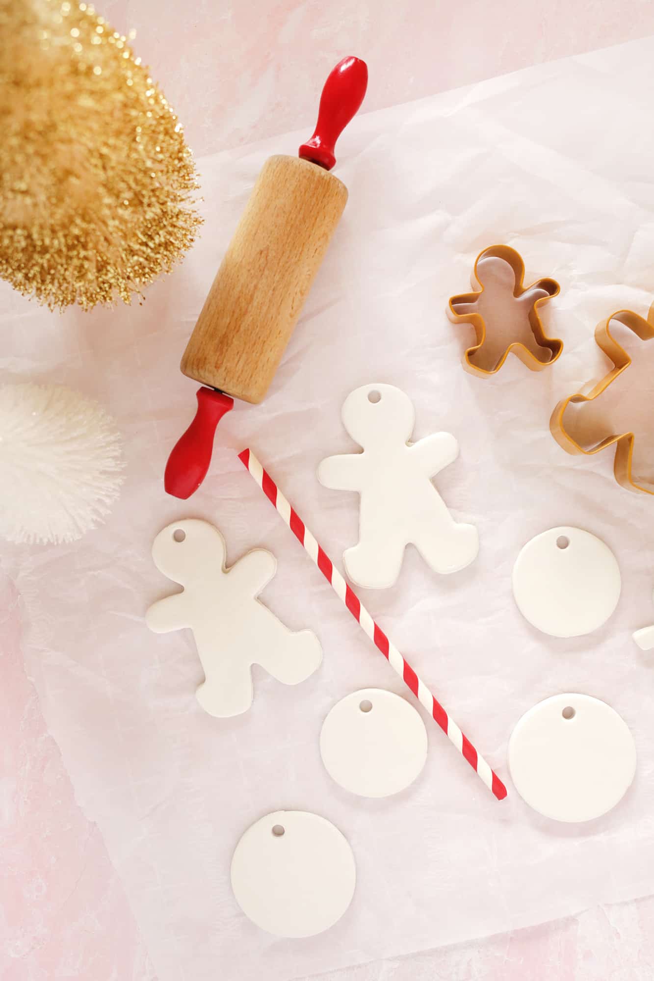 gingerbread people and circle ornaments made from clay with a rolling pin and red and white straw by them