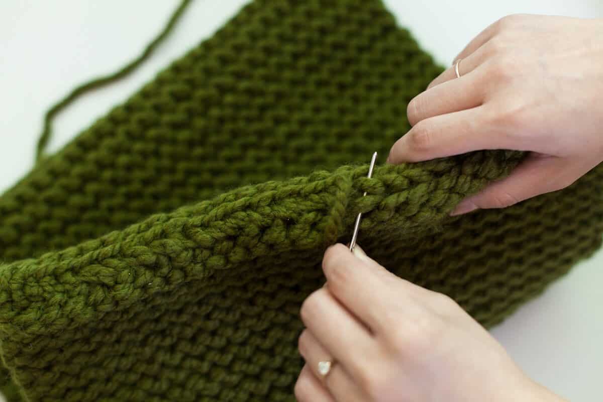 someone putting a sewing needle through the green knitted rectangle