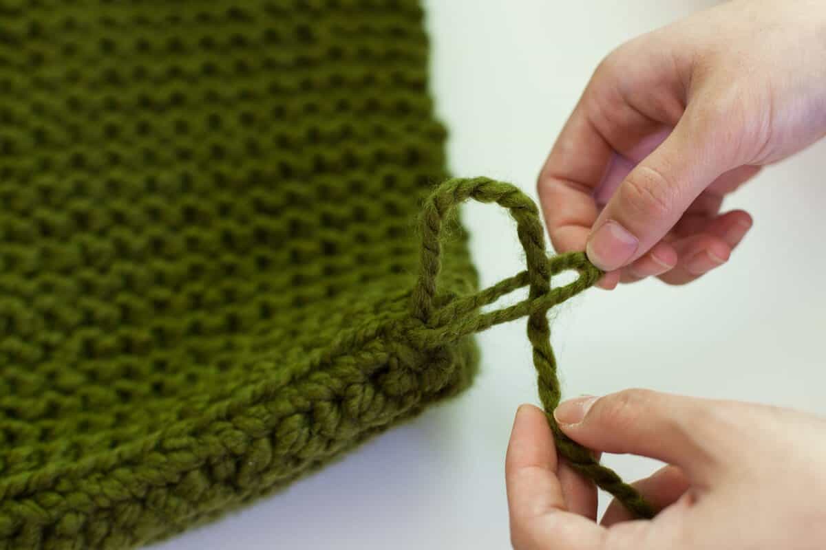 someone tying the string of the green knitted rectangle