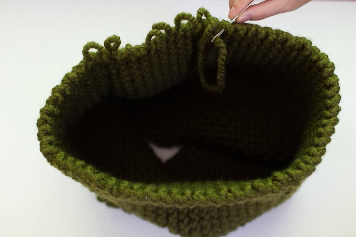 the green knitted rectangle in a cone with someone sewing it together