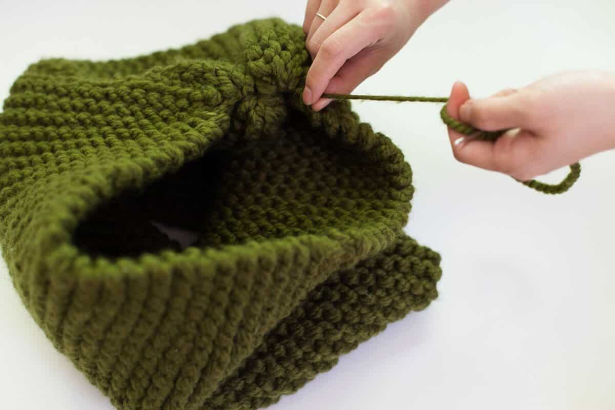 a green knitted cone with someone pulling a string tight