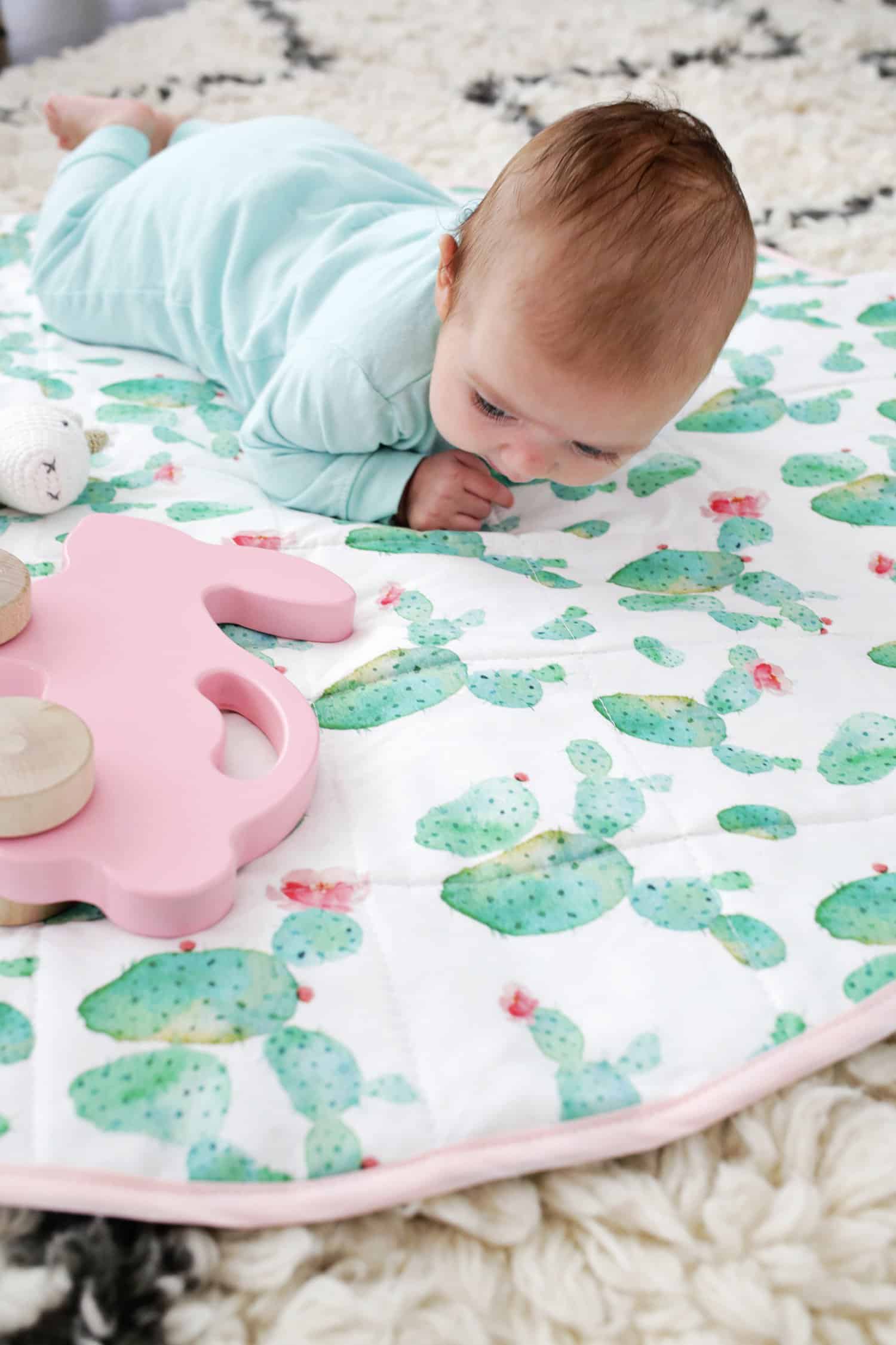 close up of baby on round quilted mat with wooden pink bunny on wheels and stuffed horse