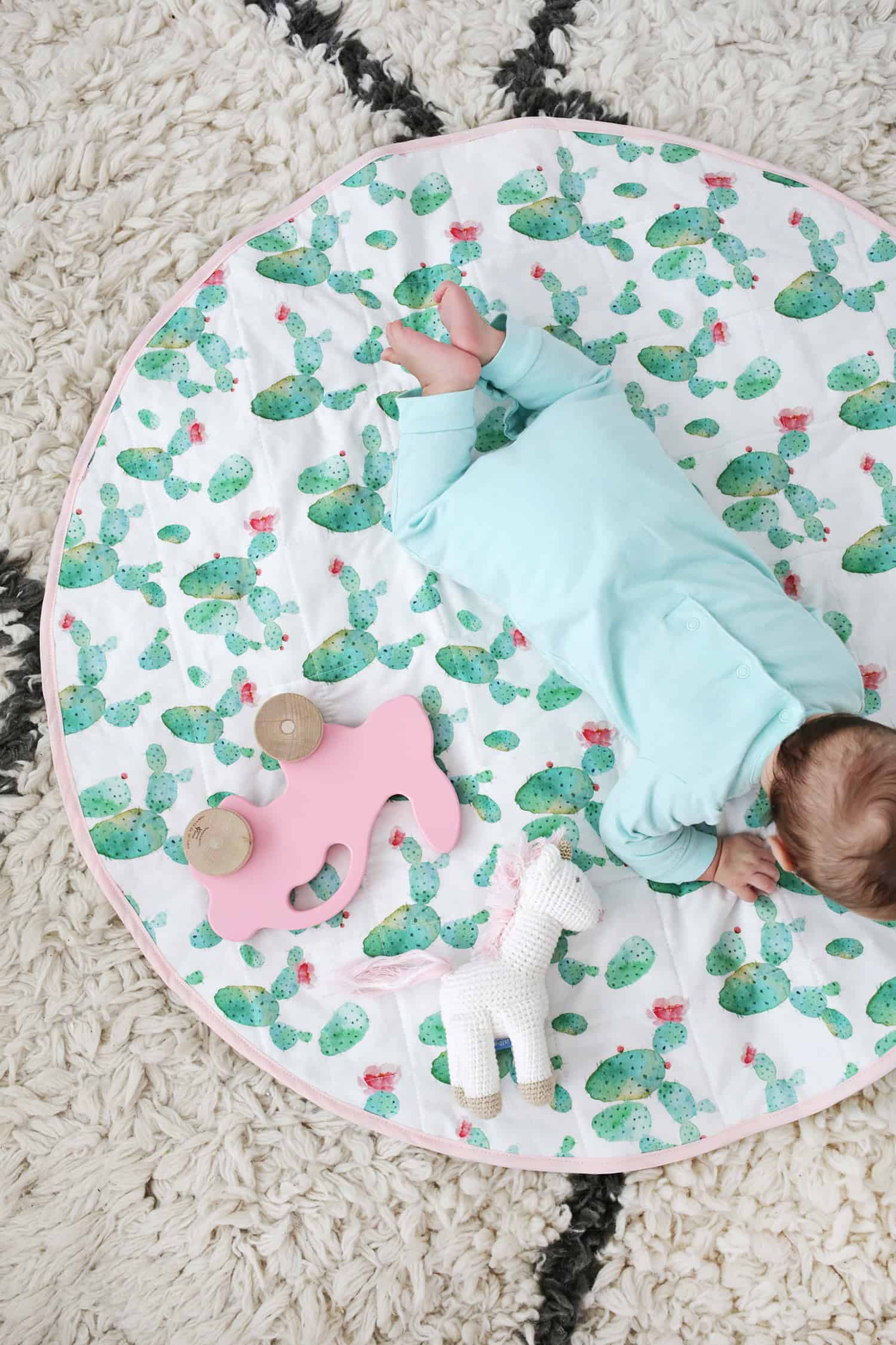 baby on round quilted mat with wooden pink bunny on wheels and stuffed horse