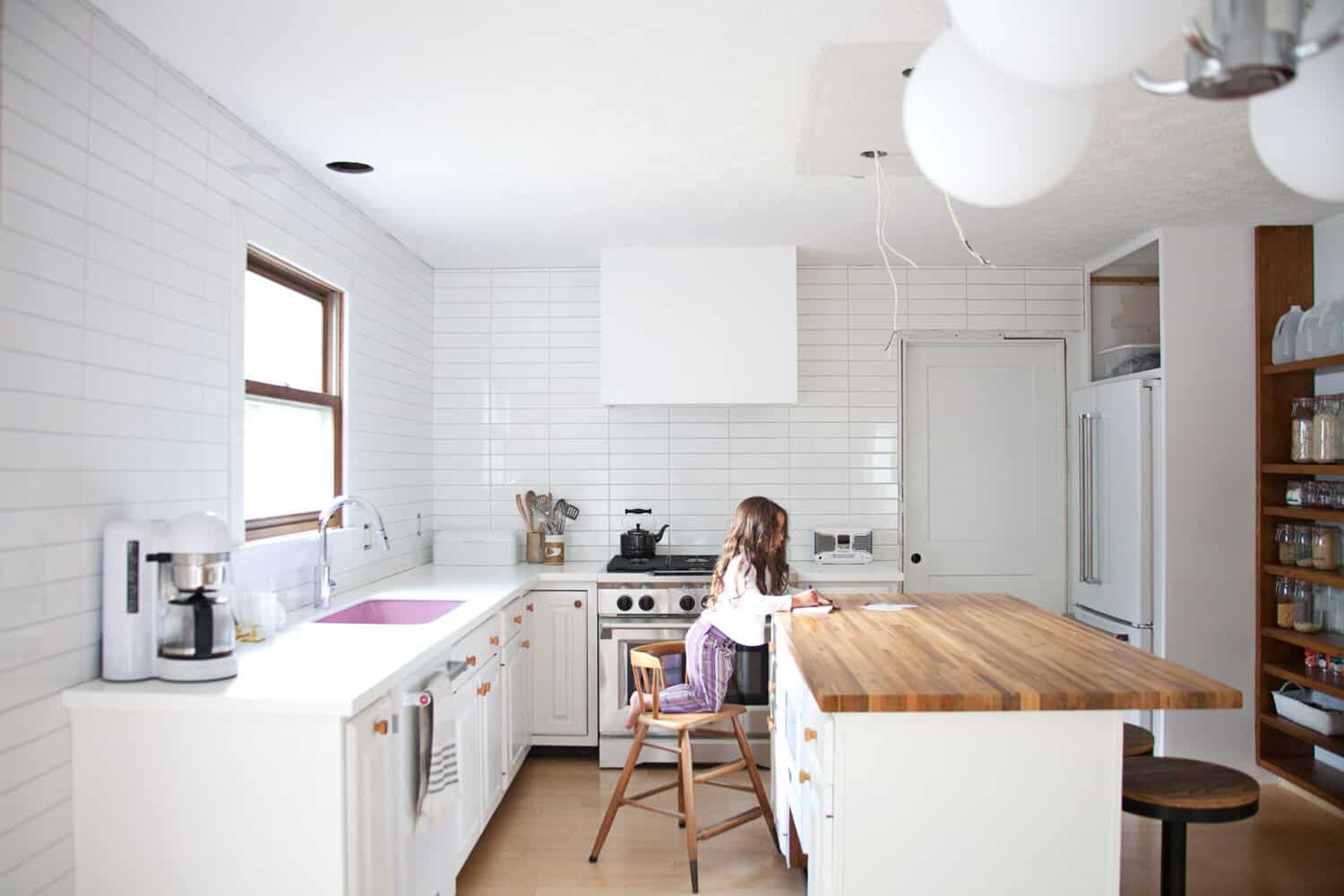 a child sitting at the island in the white kitchen with the white modern hood vent cover over the stainless stove