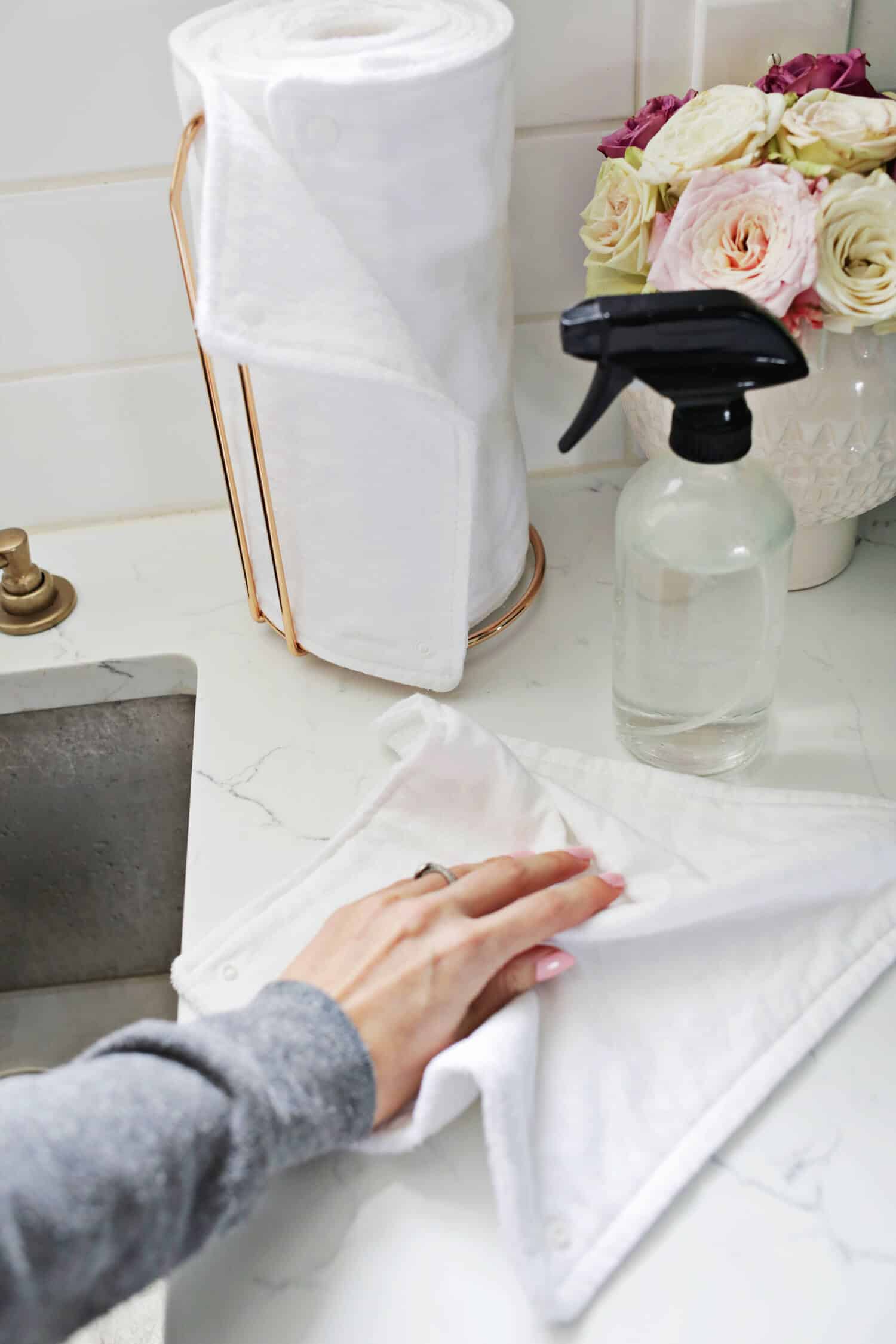 unpaper towels on towel holder with spray bottle and vase of flower next to it and someone cleaning the counter