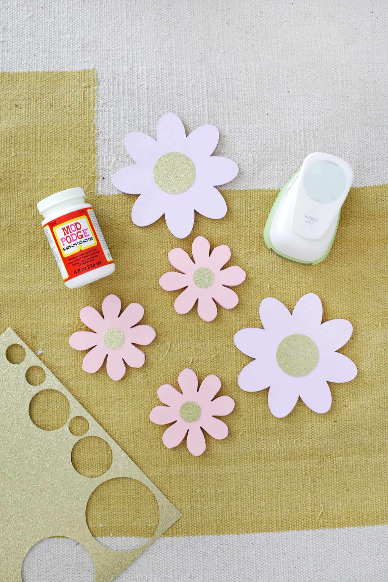 5 painted wooden flowers with mod podge and a circle cutter next to them