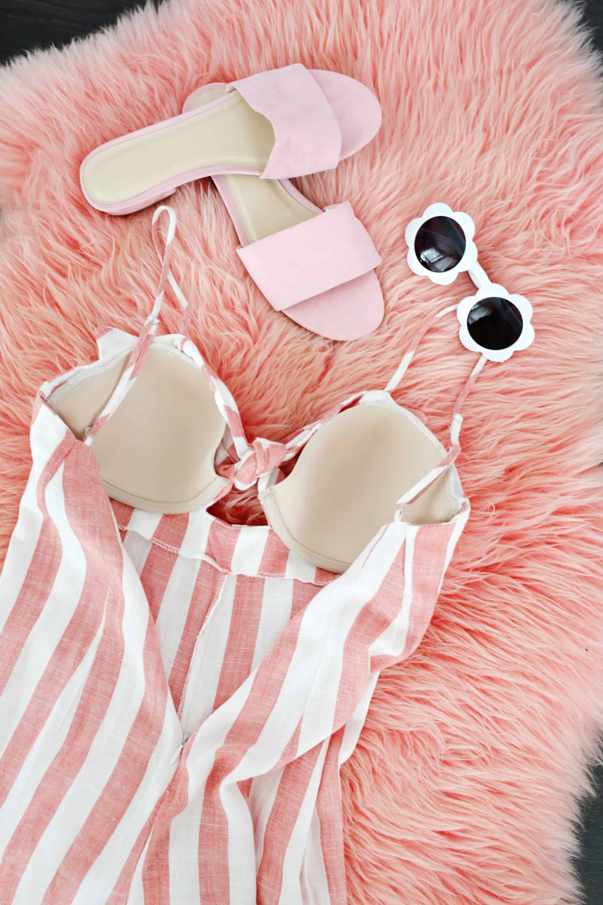 a pair of pink sandals, white flower sunglasses, and a pink and white stripped dressed with built in bra in it laying on a pink fluffy rug