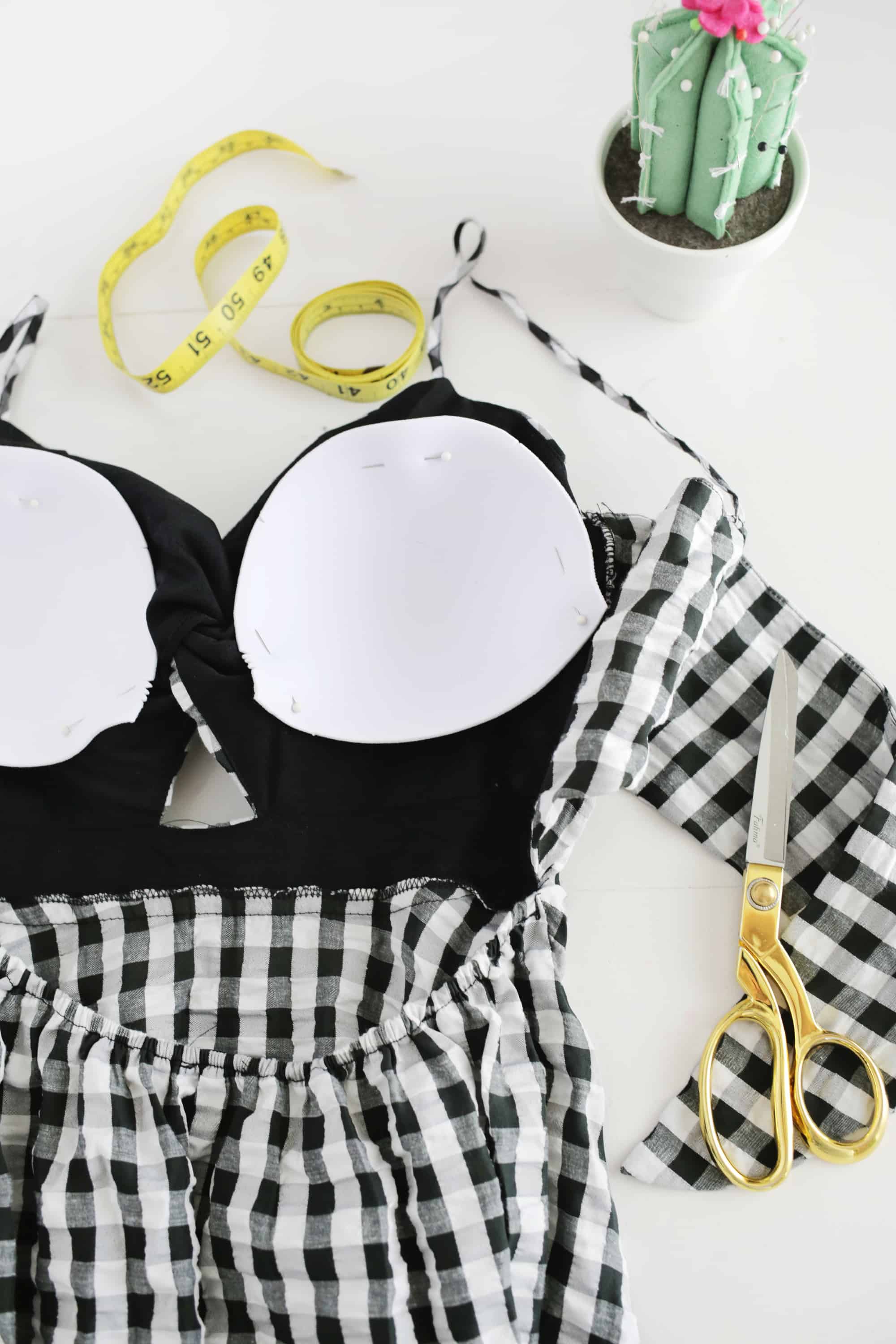 a white and black checkers dress with bra cups pinned into it and gold scissors laying next to it