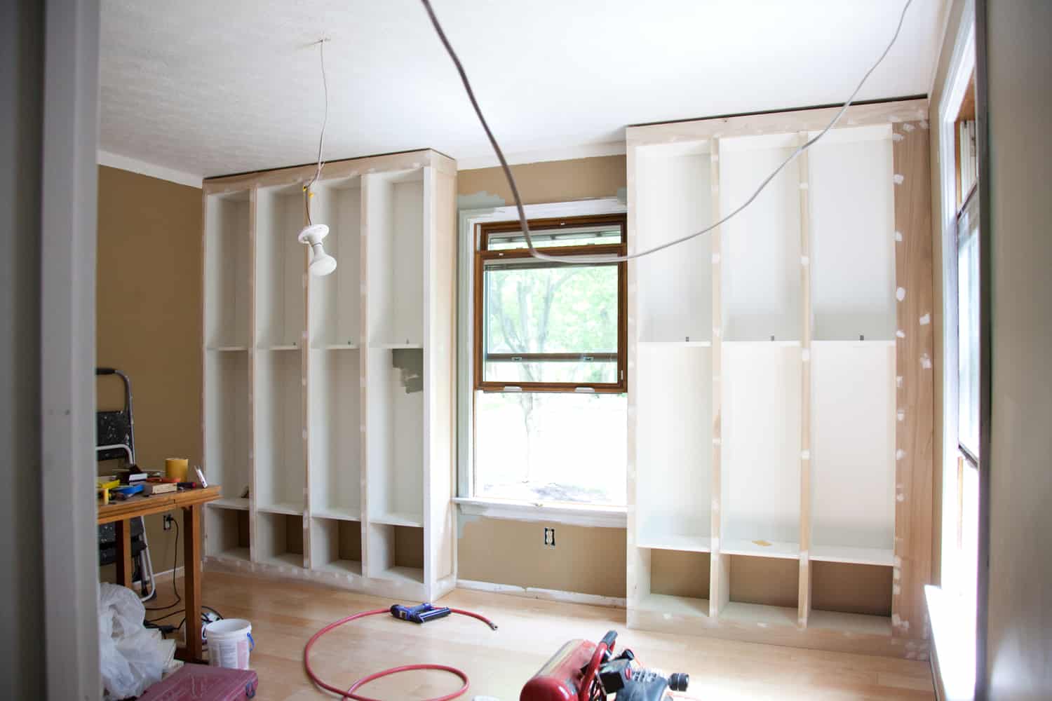 unfinished bookcases against wall with light fixture hanging down in front of it and powertools on floor