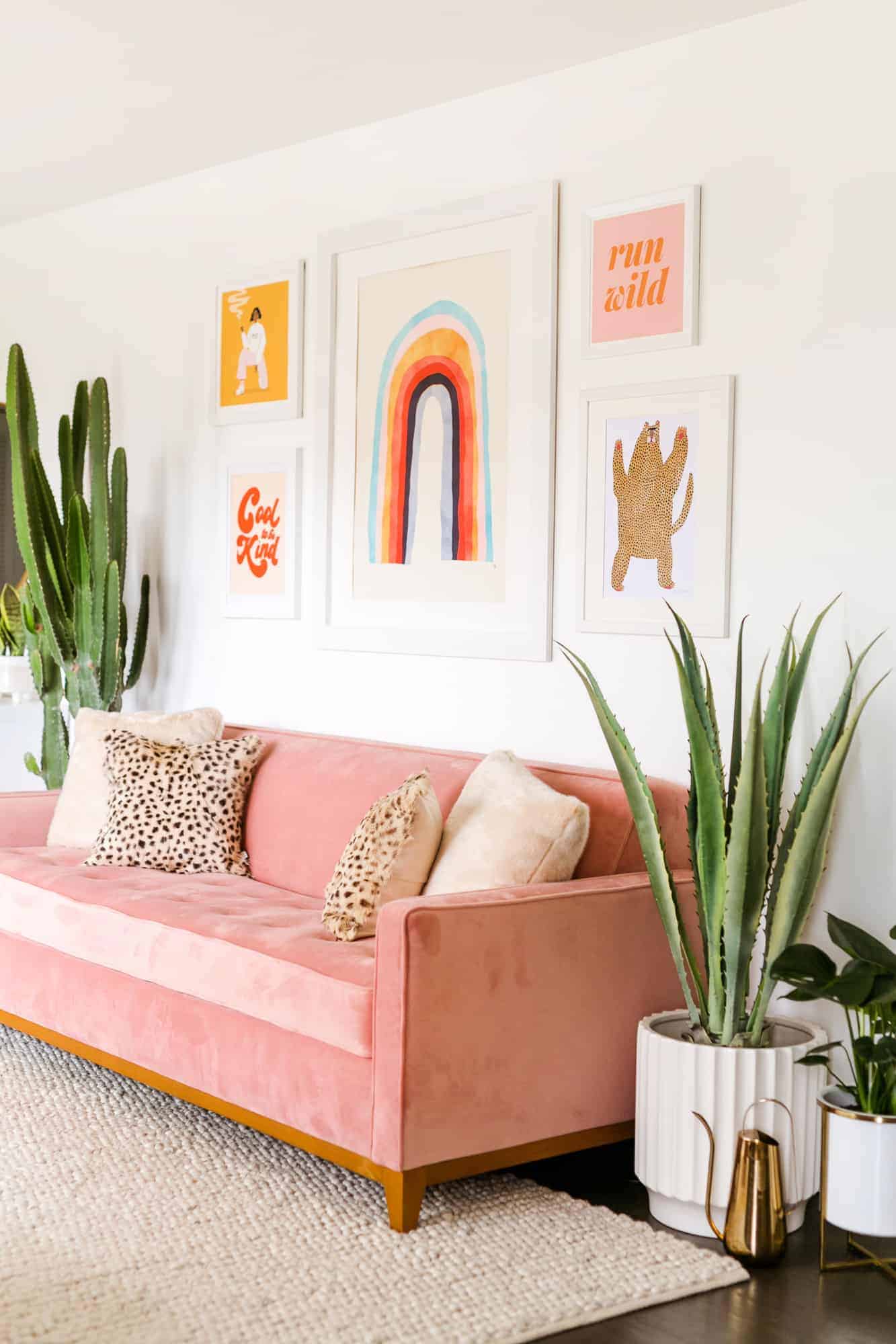 a pink sofa with 4 cushions on it and 5 art pictures hanging above it on the wall