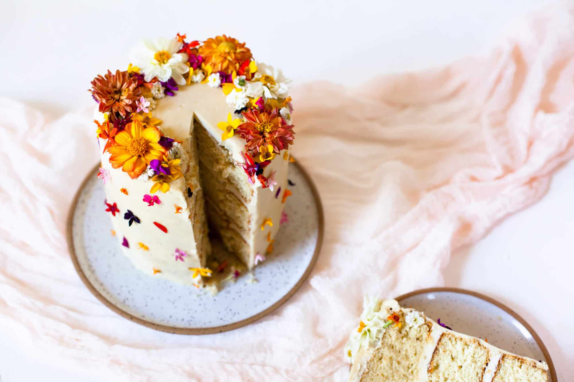 a white cake with edible flowers on it with a piece missing