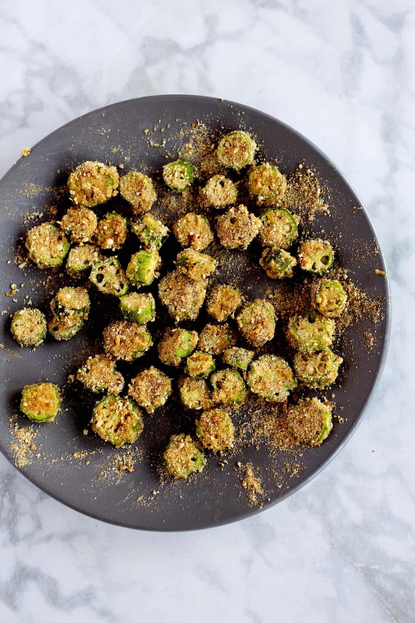cut up okra on black plate with bread crumbs sprinkled over it