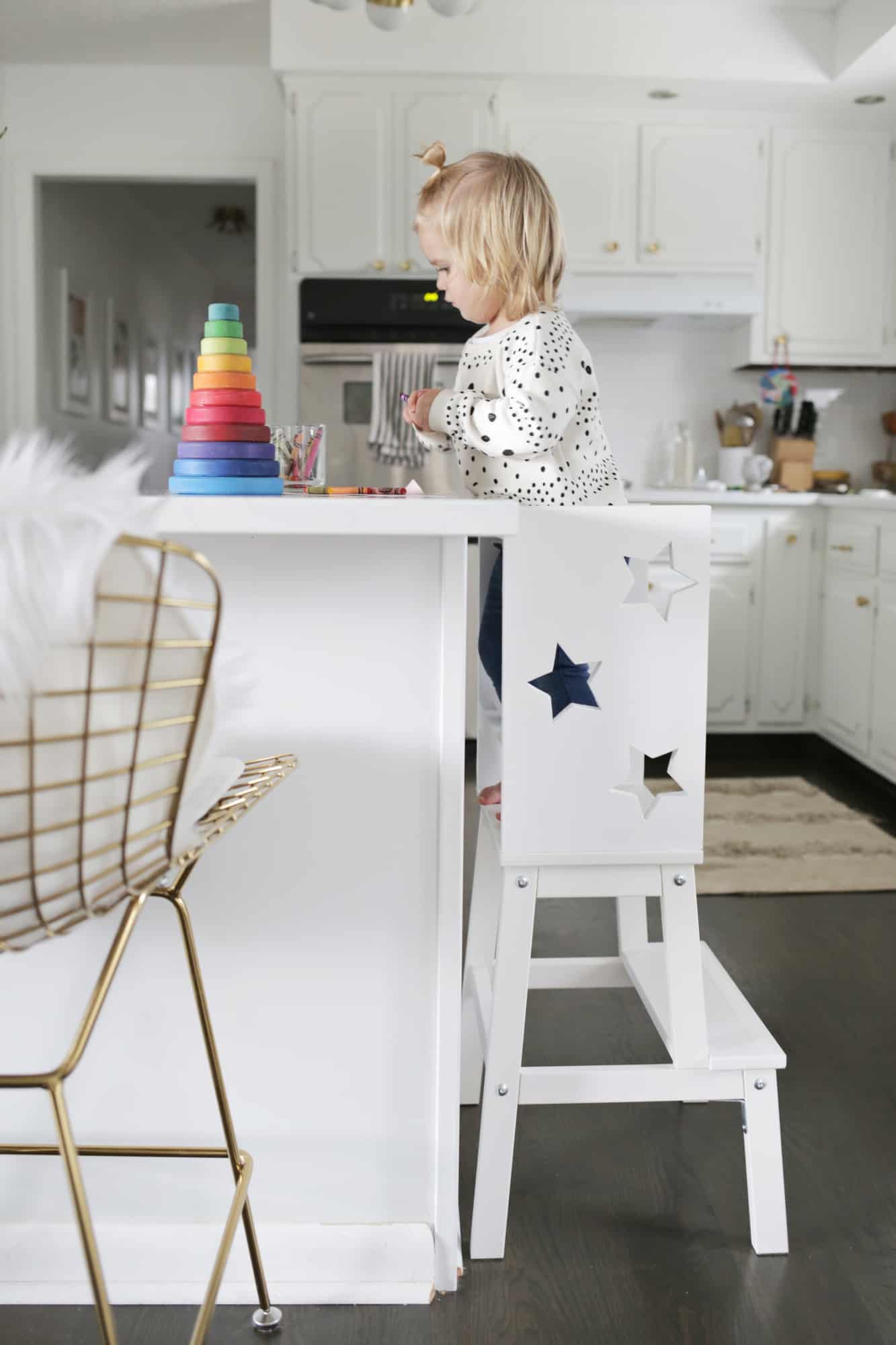 toddler standing on star step stool in front of kitchen island playing with toys