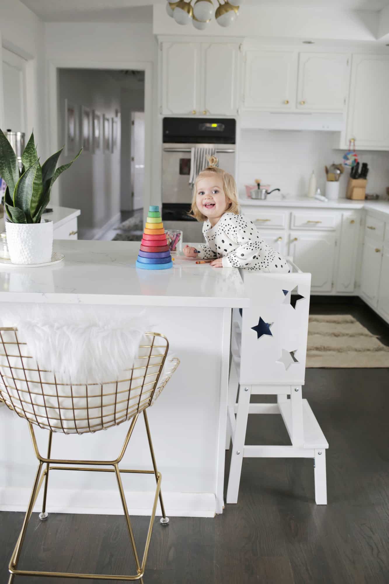 toddler smiling at camera while on star step stool coloring on kitchen island