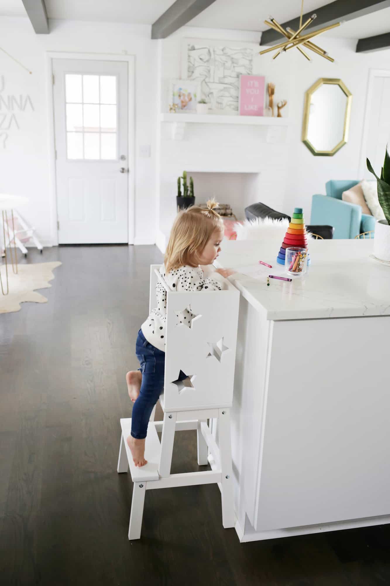a toddler climbing up the star step stool by a kitchen island with toys on top
