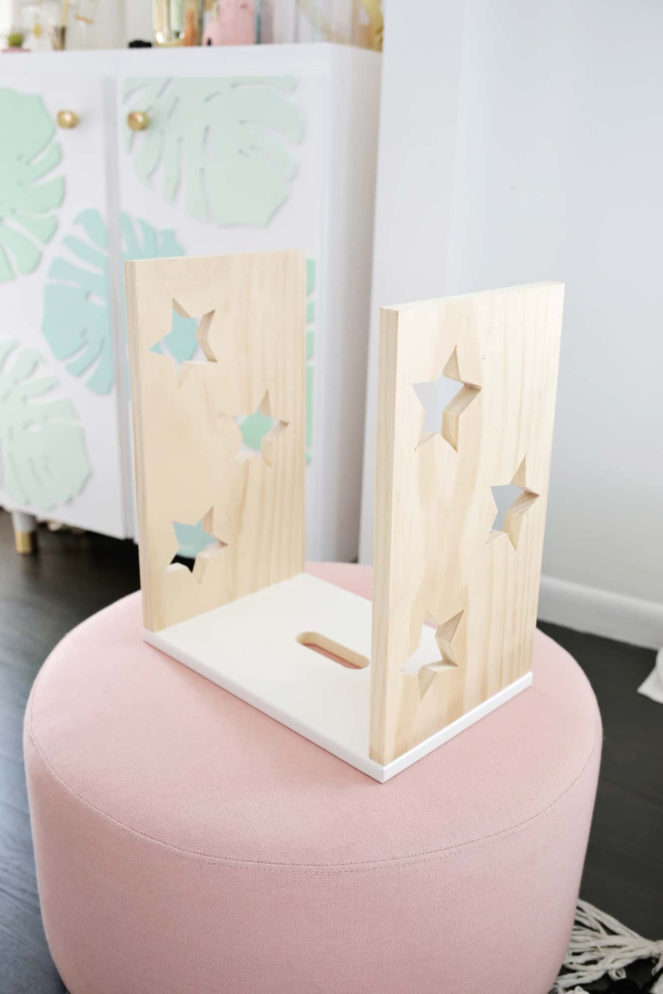 3 pieces of rectangle wood nailed together with 3 stars cut out on 2 sides on a pink ottoman