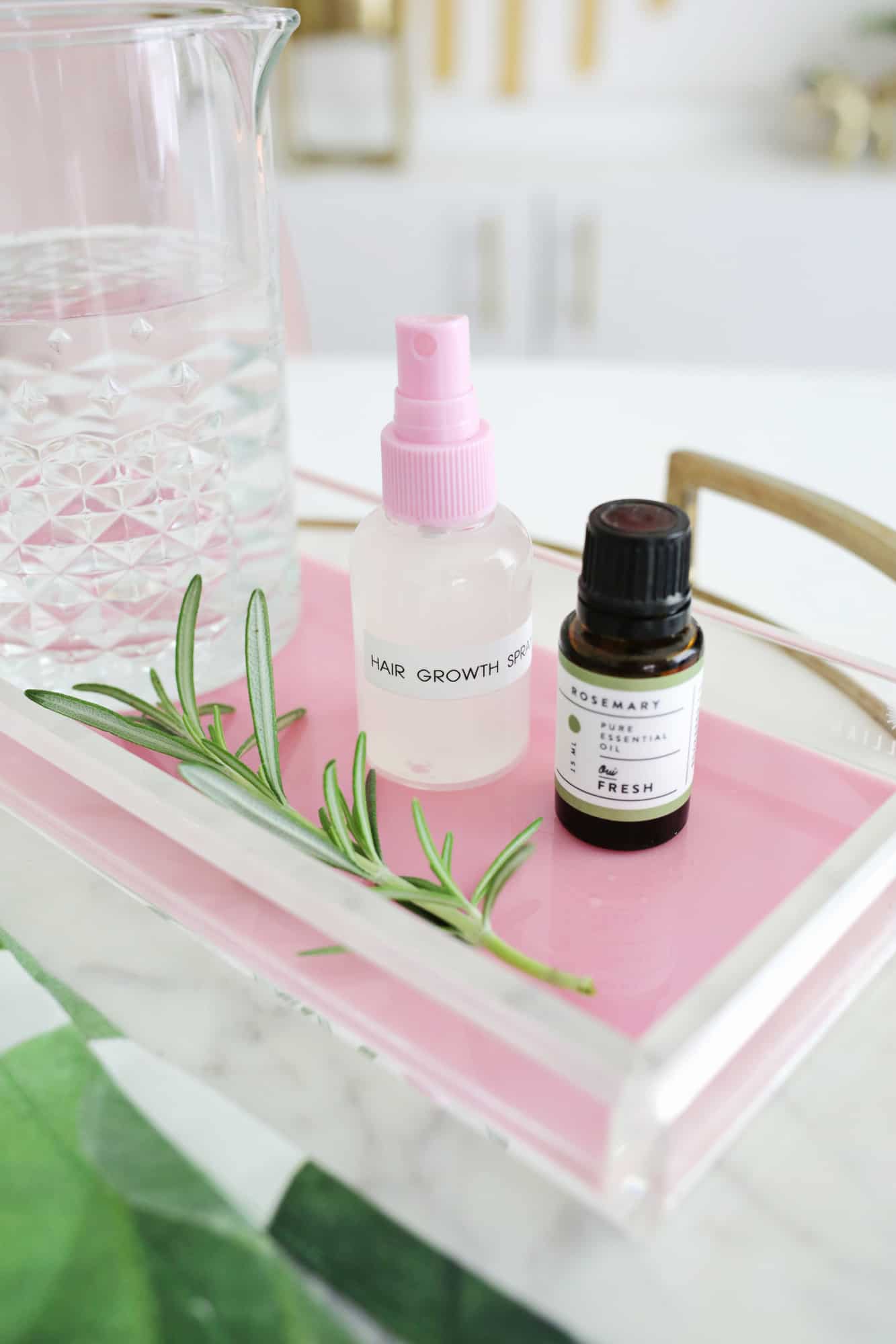 a tray with a glass of water, a spray bottle labeled hair growth spray, and a bottle of Rosemary essential oil on it