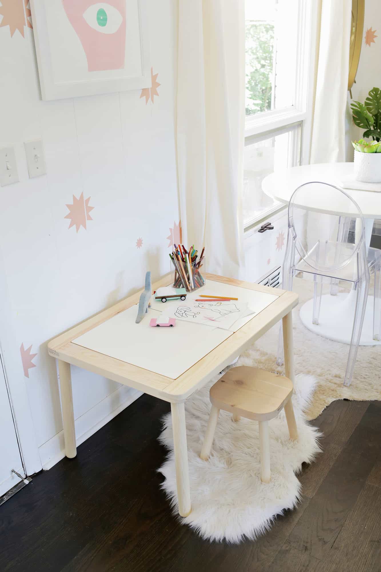 closed wooden sensory table with colored pencils and drawings on it with a  wooden stool on a white rug