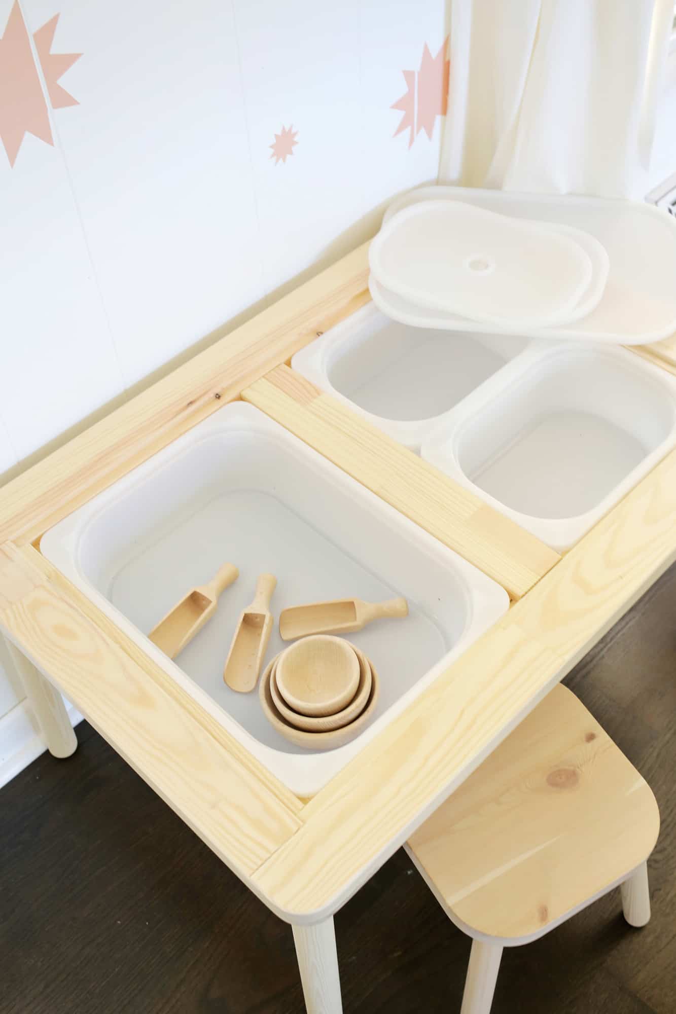wooden sensory table with white bins in it and wooden scoops and wooden bowls