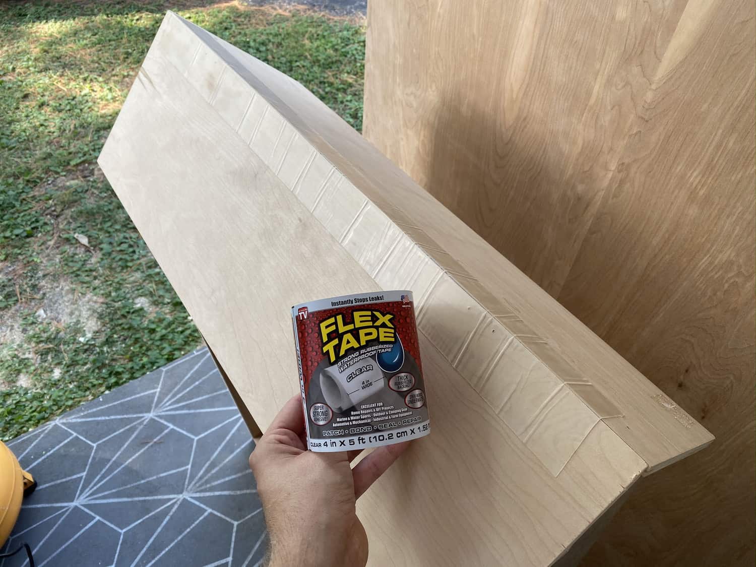 someone holding a roll of flex tape in front of the unfinished roof of the dollhouse