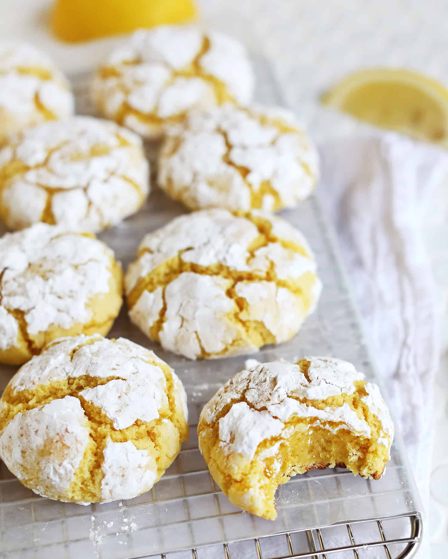 lemon burst crinkle cookies on a cooling rack with one cookie having a bite taken out of it