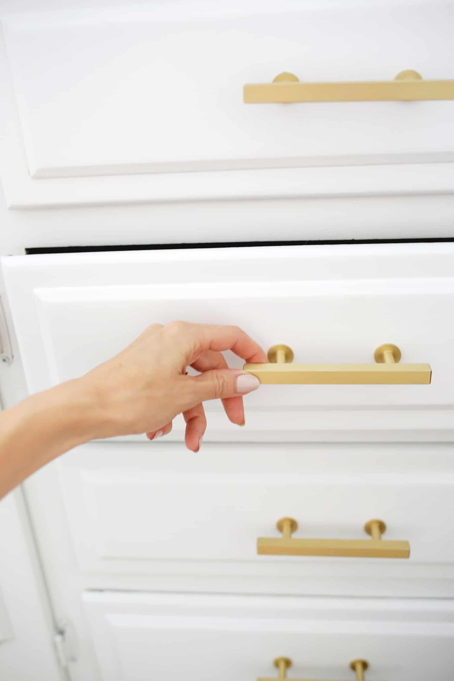 someone opens a white cupboard with gold handles