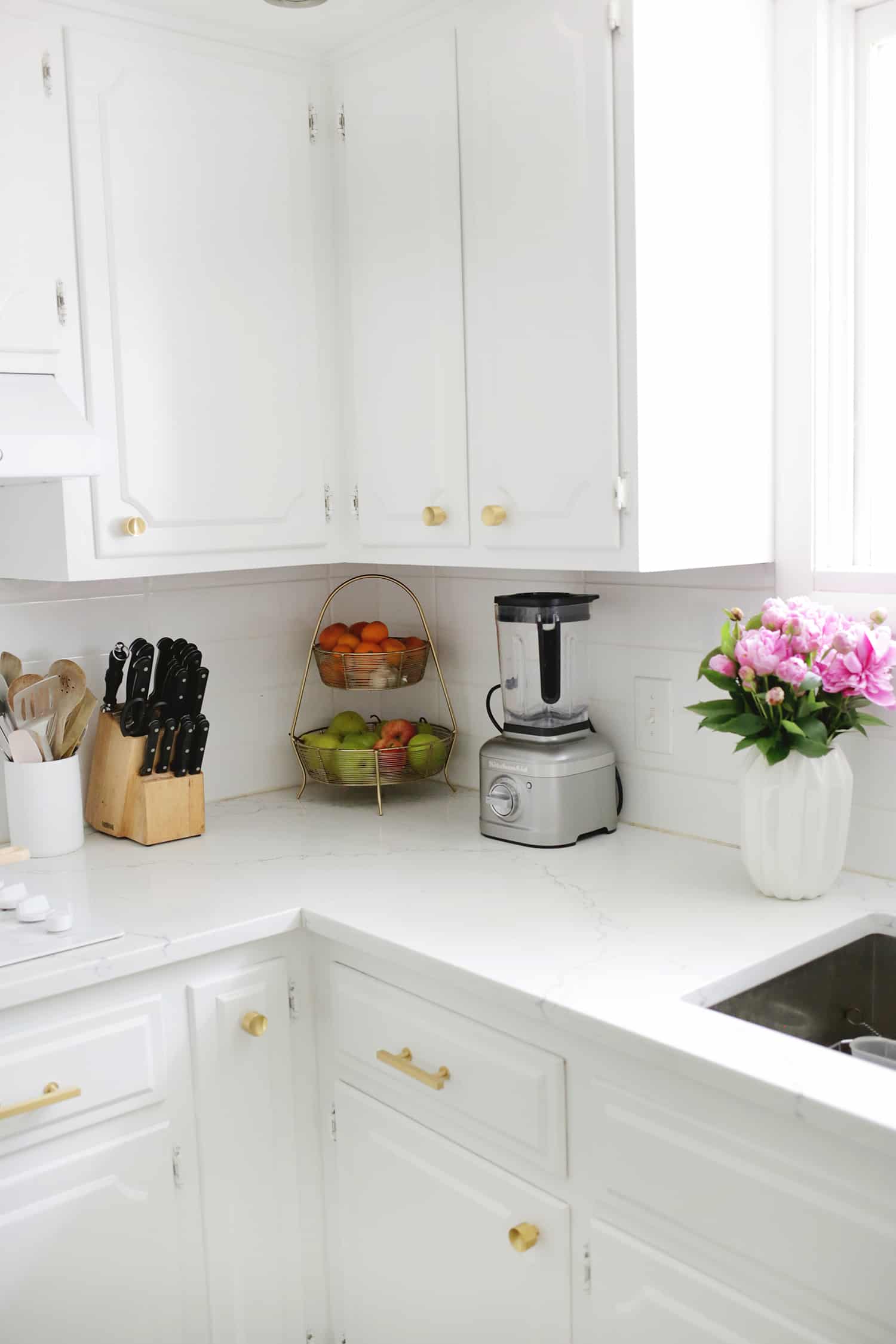 white kitchen with knives, fruit, blender, and flowers in a vase on white countertop