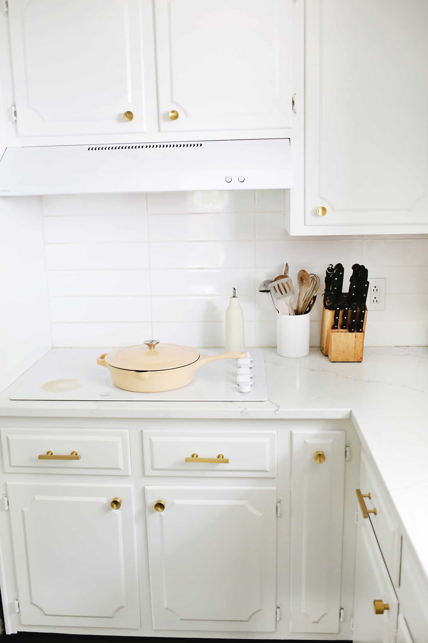 vitt kök med vit spishäll och en persikopanna ovanpå