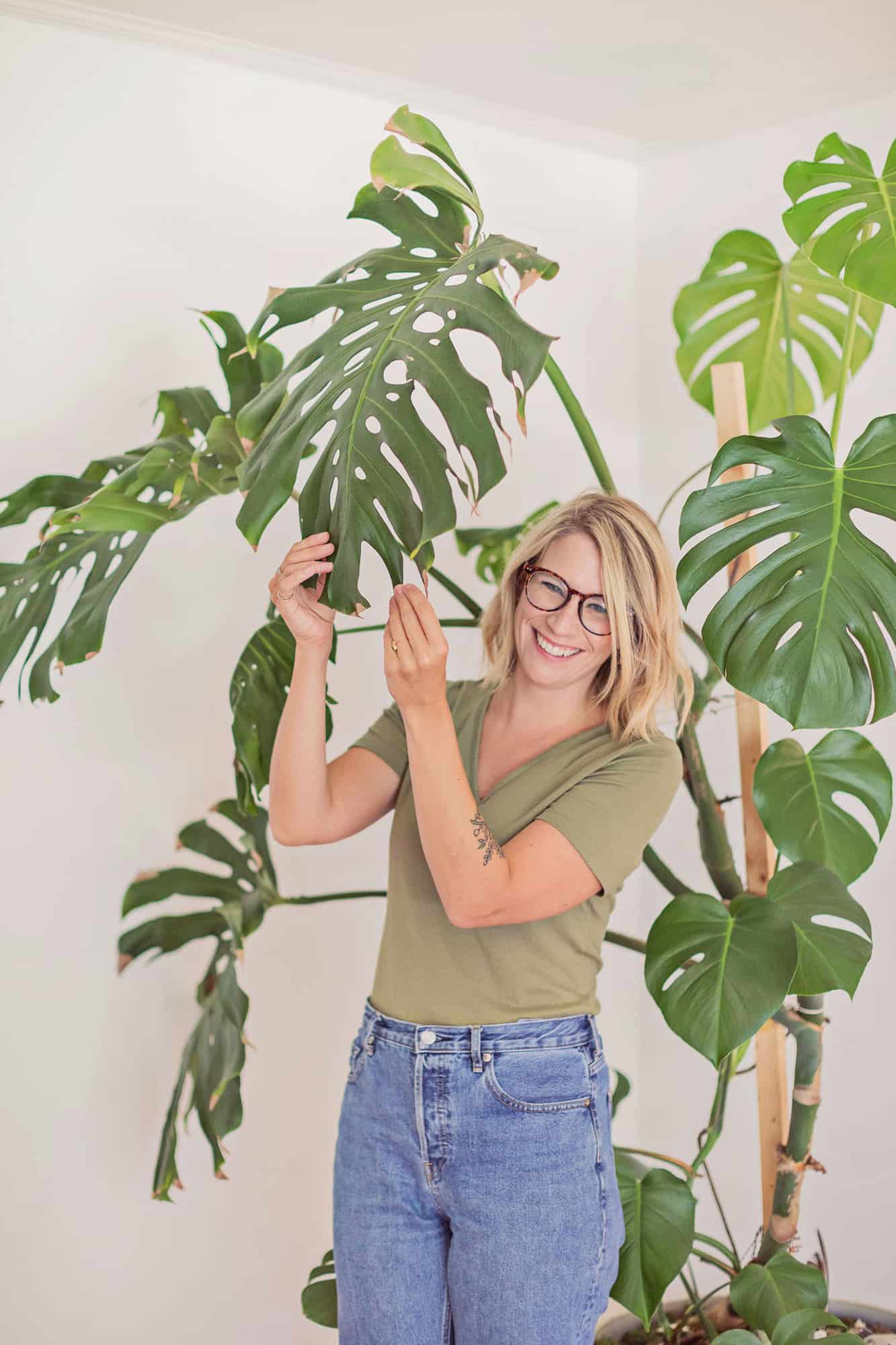 a woman in a green t-shirt holding the leaves of a monster plant