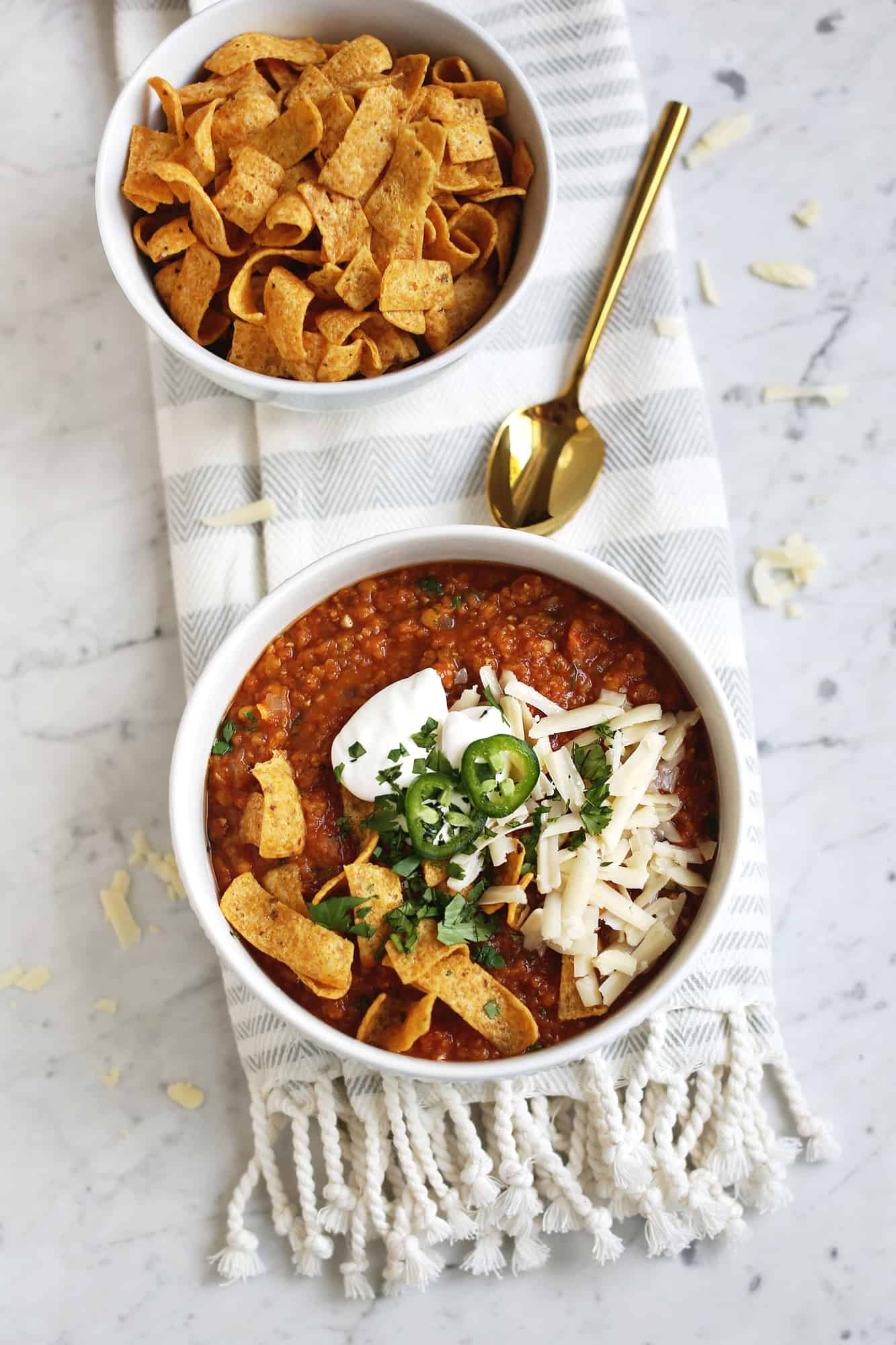 red lentil vegetarian chili in a white bowl with a gold spoon and a bowl of fritos next to it