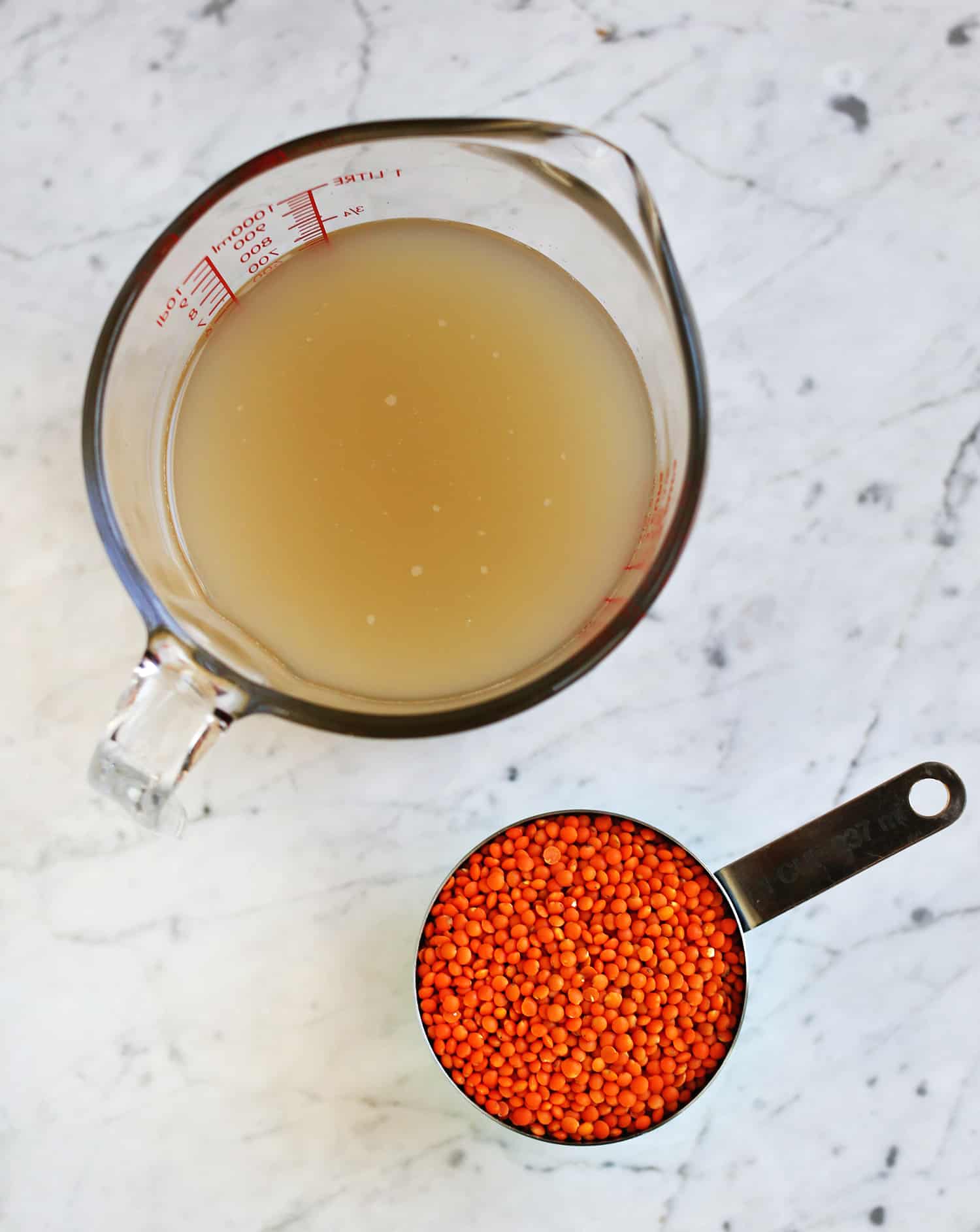 a glass measuring cup of chicken broth and a measuring cup of red lentils