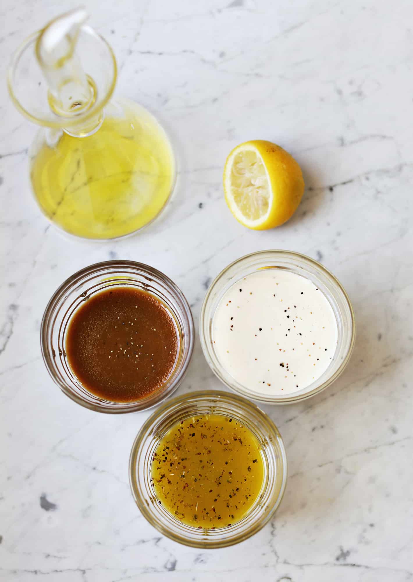 3 glass bowls of sauces, half a lemon, and a glass bottle of yellow liquid