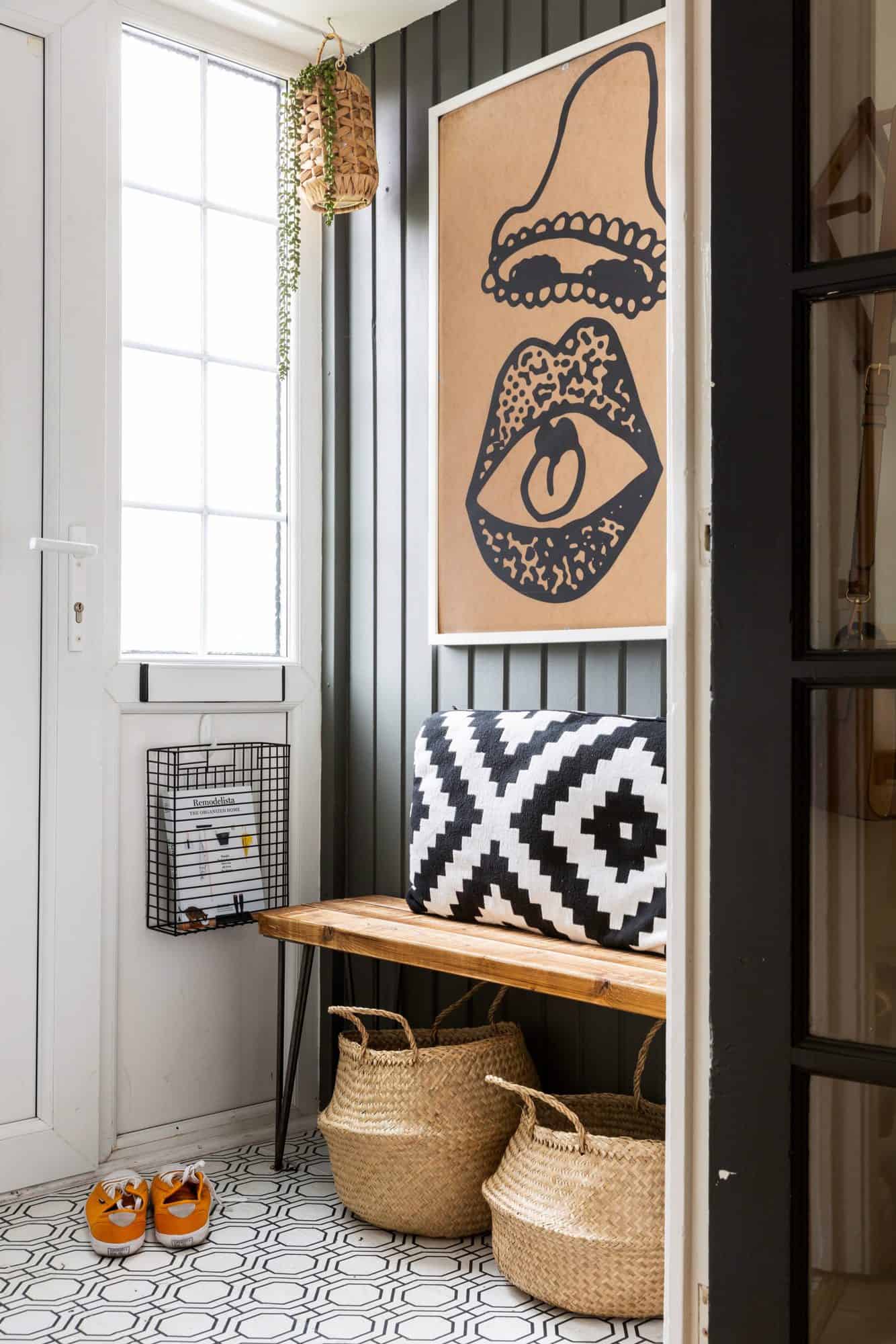 an entry way with a wooden branch and black and white pillow on it with art work hanging over it with peel and stick wallpaper on the floor