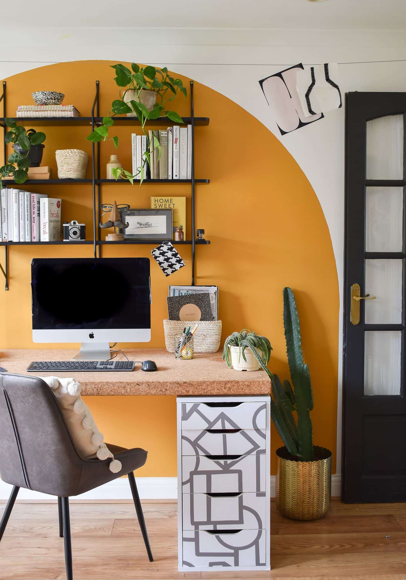 a white wall with an orange circle peel and stick wallpaper on it and shelves hanging on wall with a desk in front of it