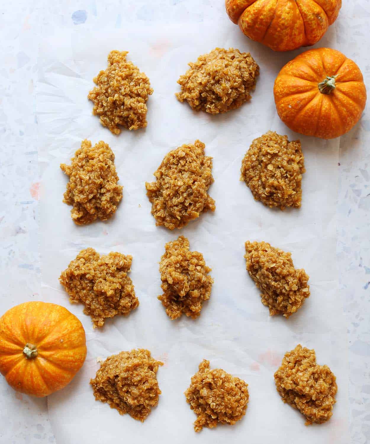 11 no bake pumpkin oatmeal cookies on parchment paper with 3 pumpkins surrounding it