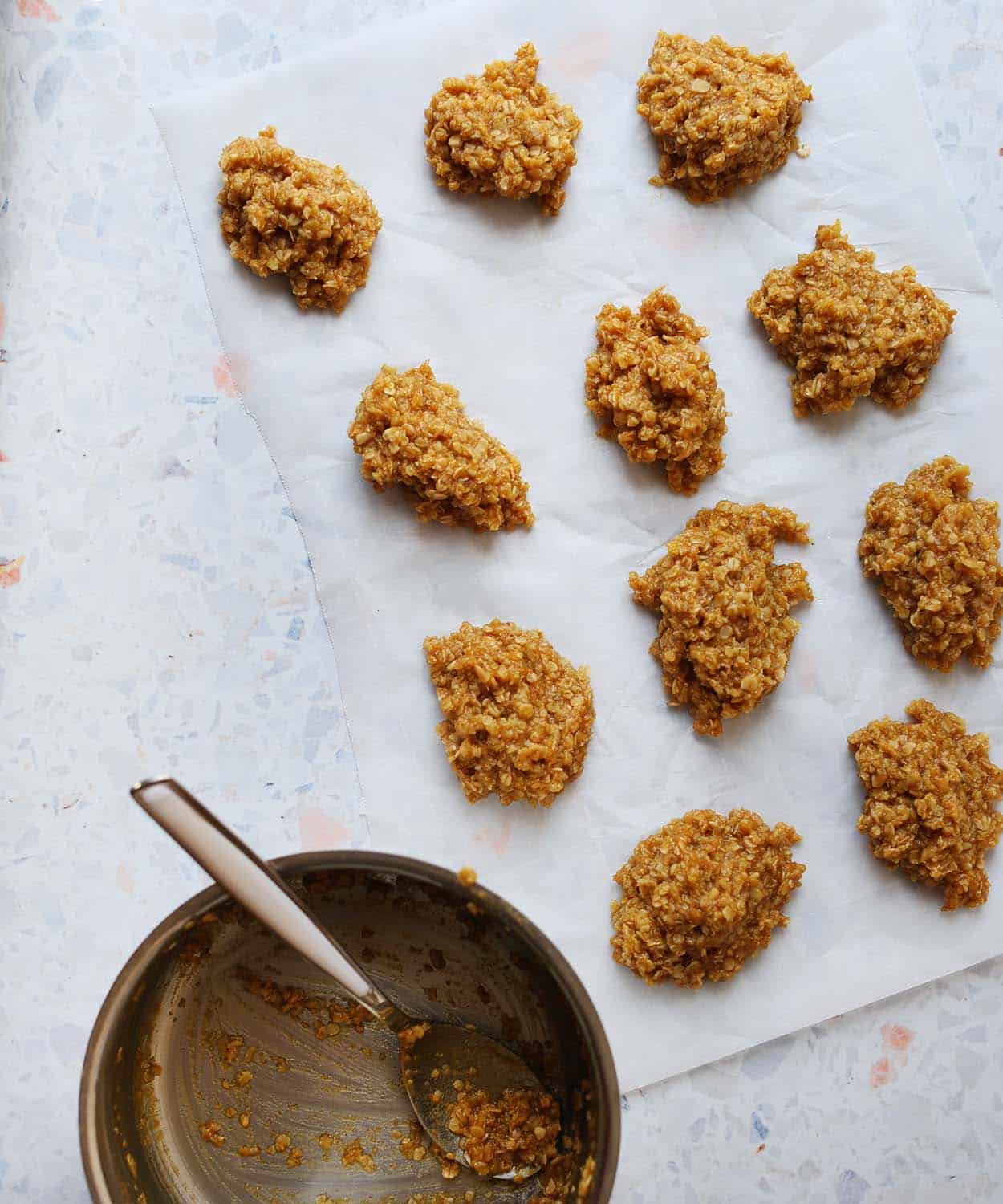 11 no bake pumpkin oatmeal cookies on parchment paper with a silver mixing bowl and spoon next to it