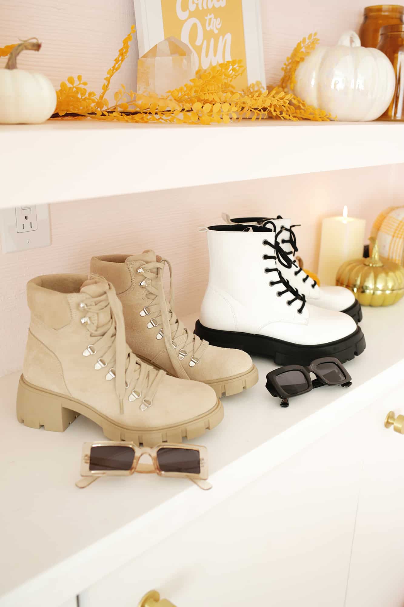 two pairs of boots and sunglasses on a fall styled bookshelf