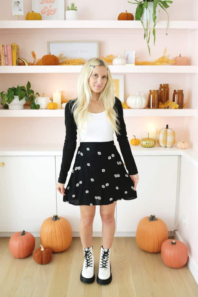women wearing a black skirt, white boots, black sweater, and hair barrettes in front of fall styled bookshelf