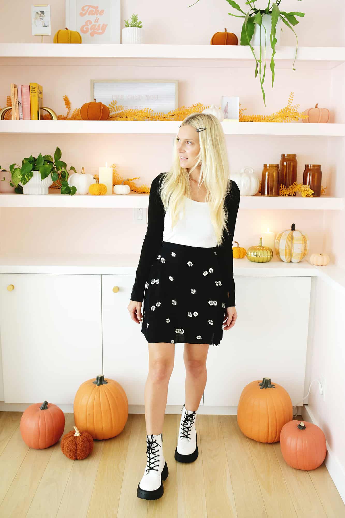 women wearing a black skirt, white boots, black sweater, and hair barrettes in front of fall styled bookshelf