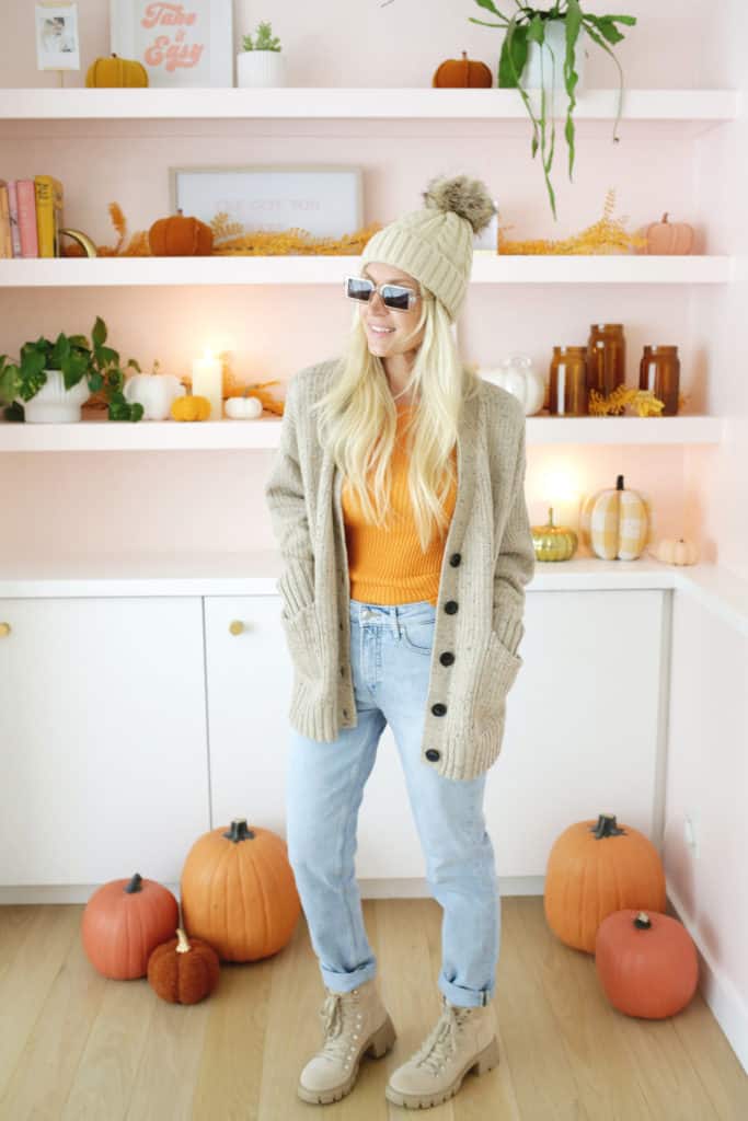 women wearing an oversized cardigan, jeans, boots, a hat and sunglasses