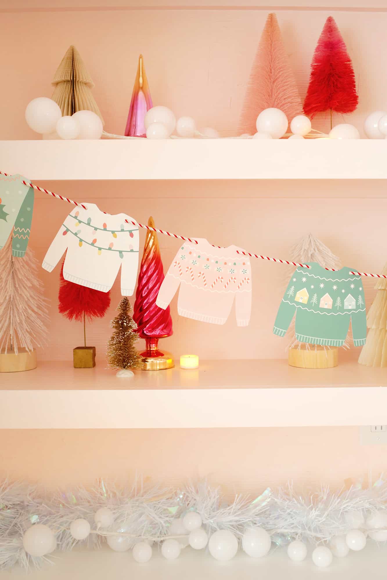 Paper Christmas sweaters strung on a garland with Christmas tree shelf decor