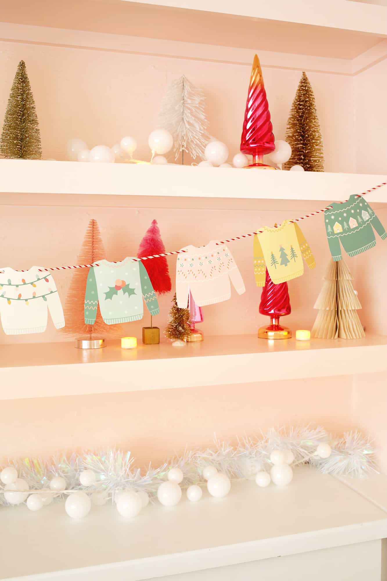 Paper Christmas sweaters strung on a twine string from a shelf with Christmas decor around it