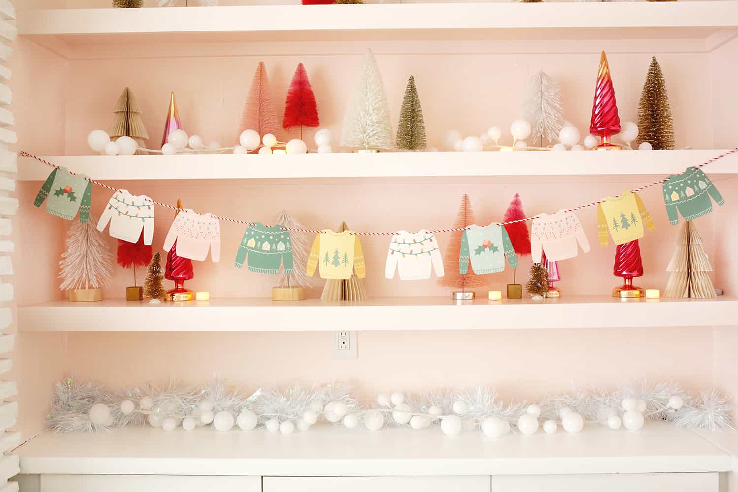 Paper Christmas sweaters strung on a garland with Christmas tree shelf decor