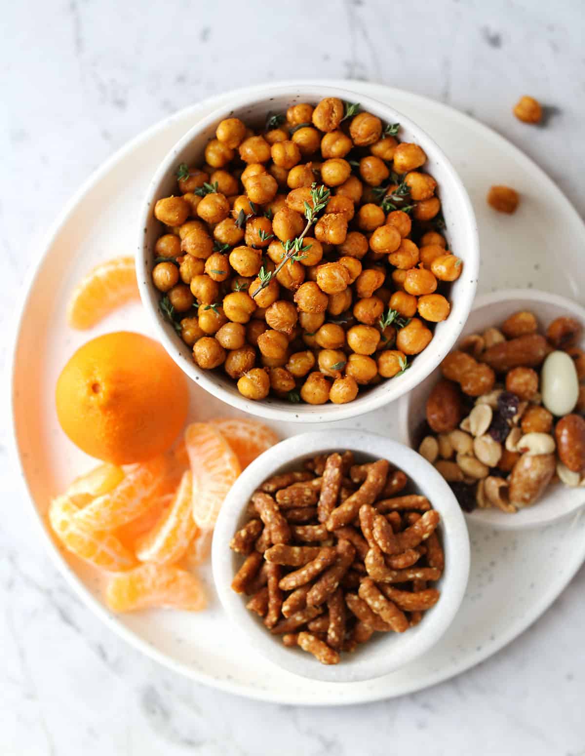 plate of snacks including a clementine, air fried chickpeas, pretzels and trail mix. 