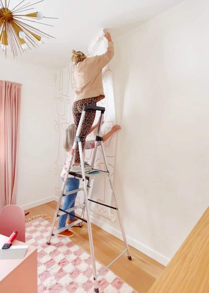 two women wallpapering an accent wall