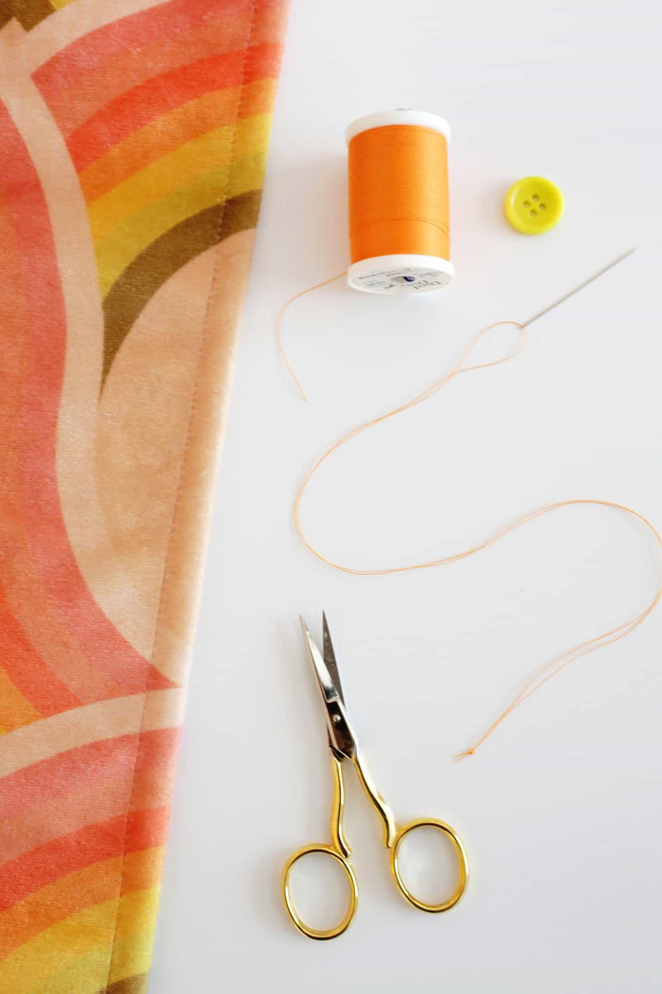 fabric, sewing needle, and thread to sew a button