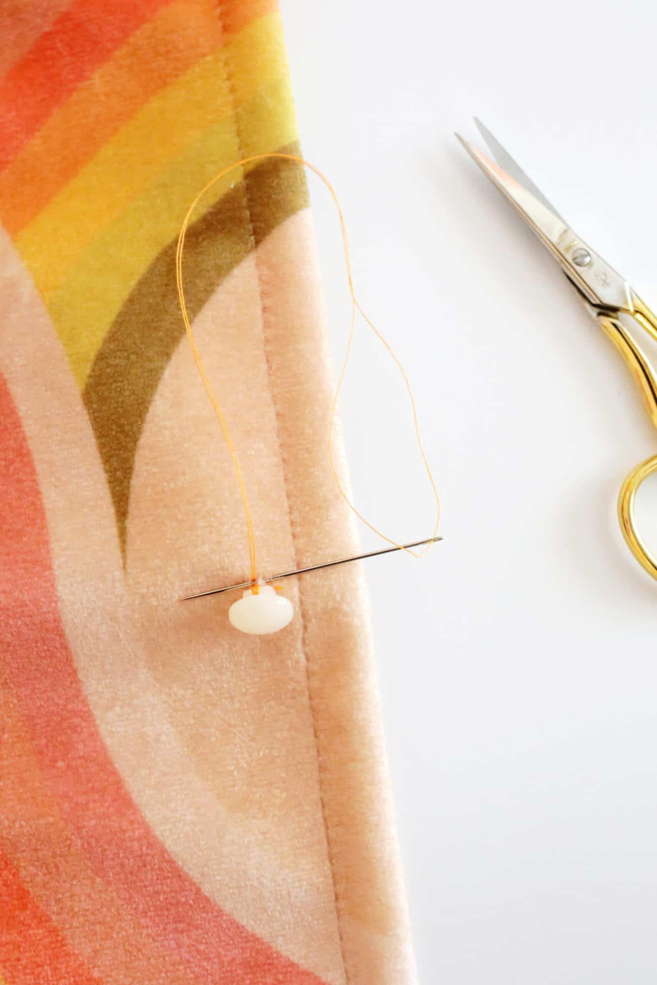 passing threaded needle through a little bit of fabric while sewing on a button
