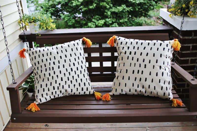 two pillows with black painted stripes and orange tassles on a porch swing. 