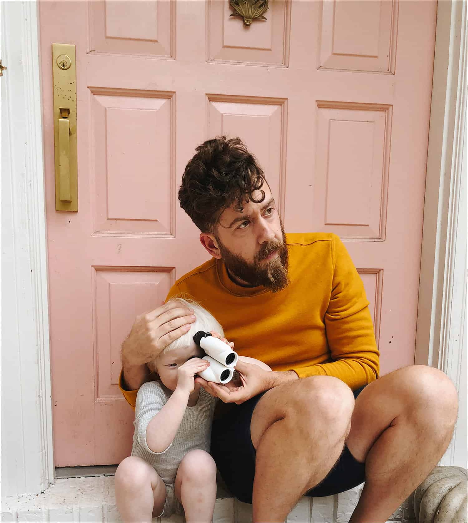 pria yang duduk di depan pintu merah muda dengan anak memegang teropong